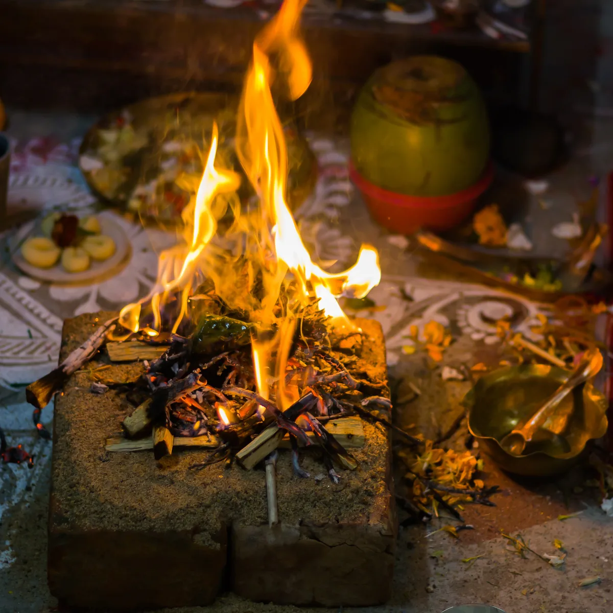 A havan kund with its fire burning, offerings and a rangoli around it