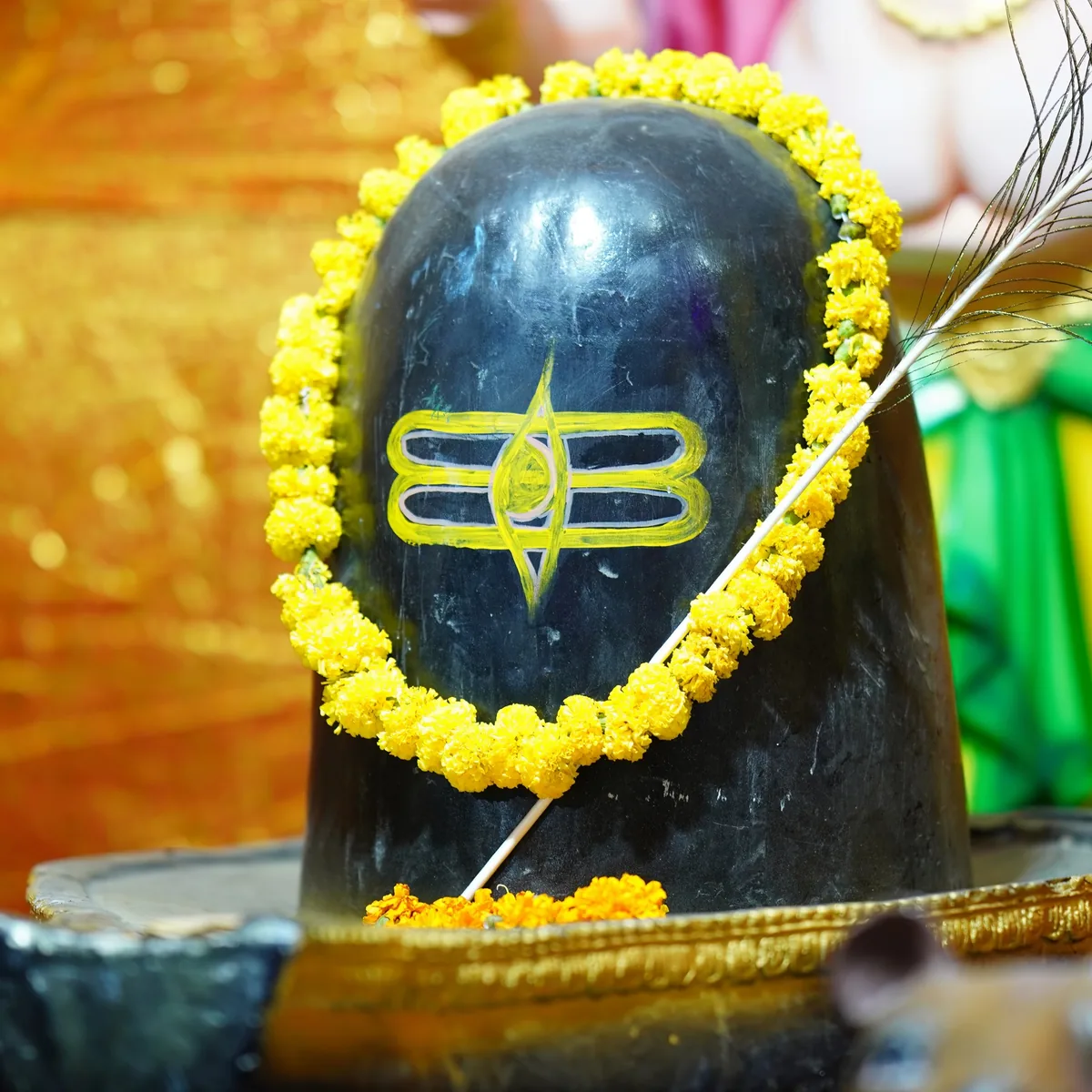 A black Shivling with a yellow garland, water pouring over it