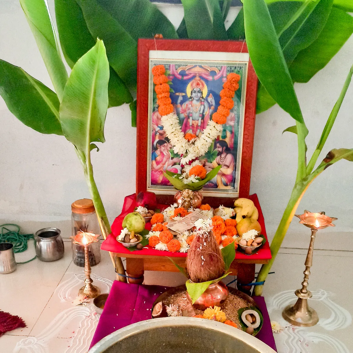 A Satyanarayan puja set up at home, with banana plants, a picture of the deity and offerings