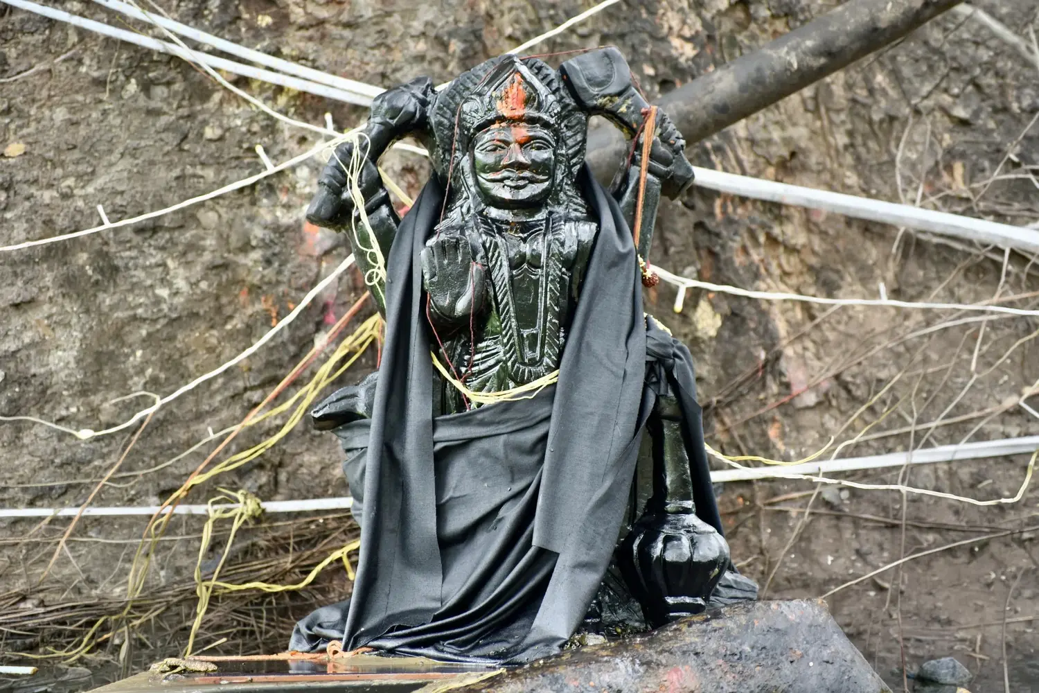 A stone idol of Shani draped in black cloth, with threads tied around it